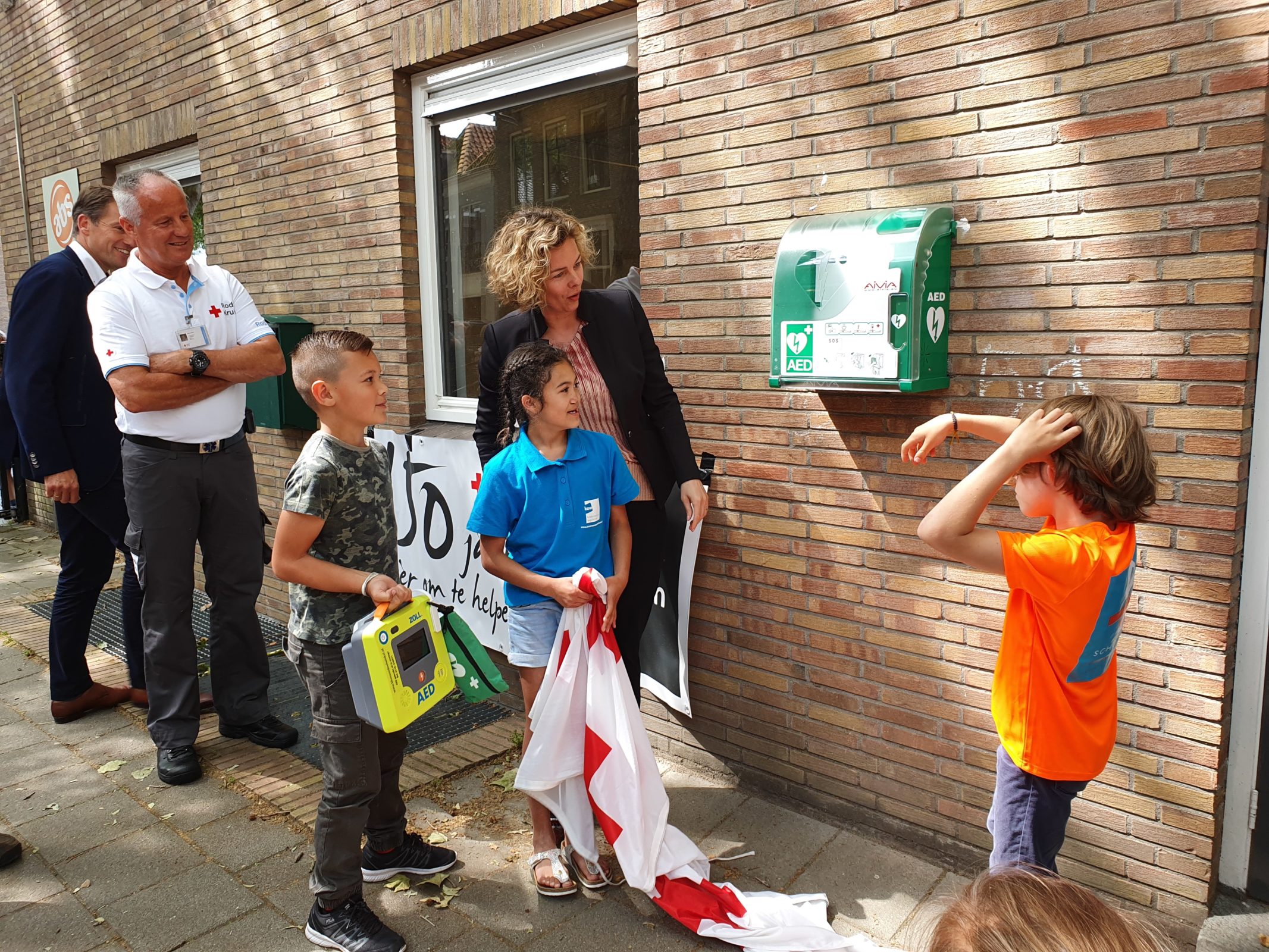 Volwassenen kijken toe hoe kinderen een AED onthullen