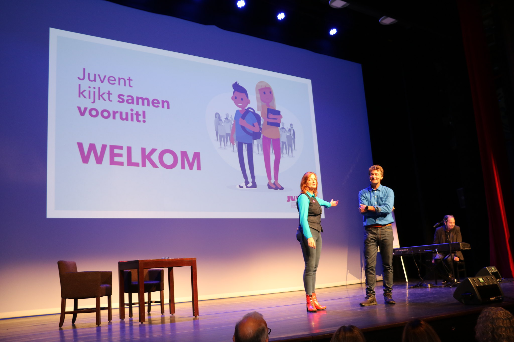 Twee sprekers op een podium verwelkomen de aanwezigen