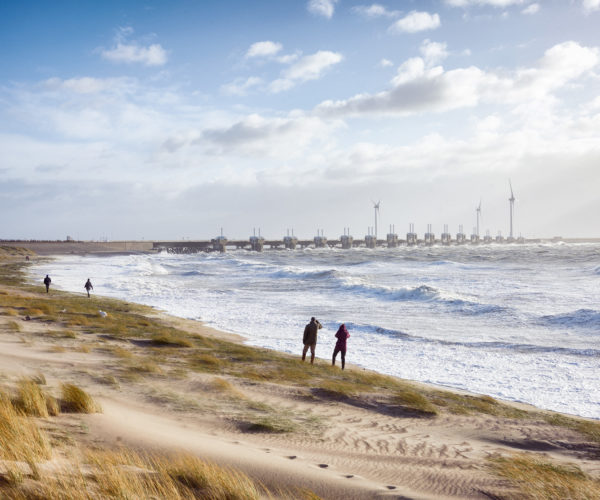 Mensen kijken naar hoge golven. Op de achtergrond de Oosterscheldekering die gesloten is