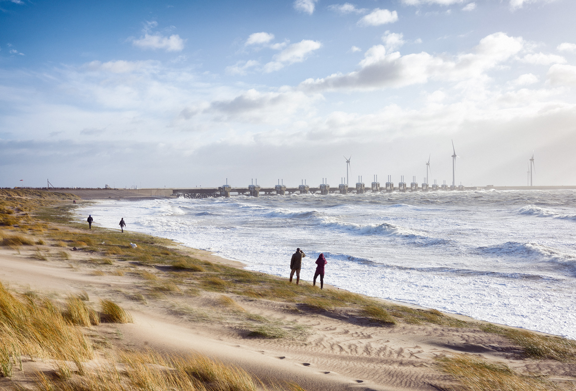 Mensen kijken naar hoge golven. Op de achtergrond de Oosterscheldekering die gesloten is