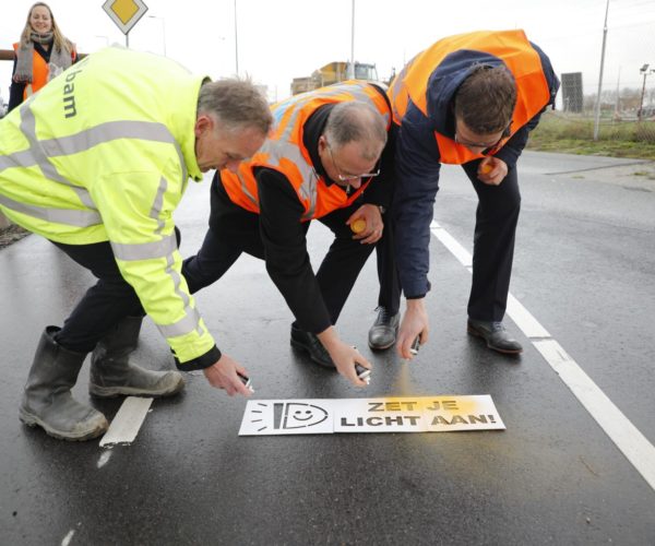 Werknemers spuiten 'Zet je licht aan!' op een fietspad bij de Nieuwe Sluis Terneuzen