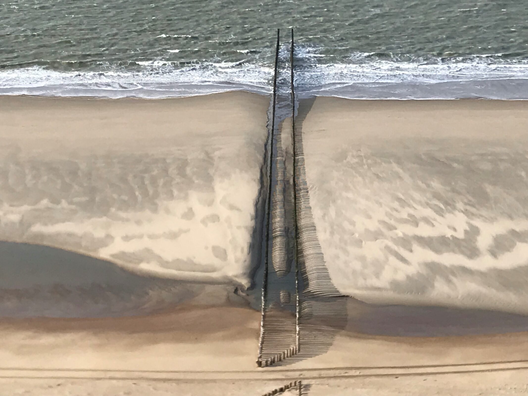 Een luchtfoto van het strand met een rij paalhoofden