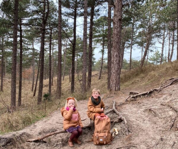 Twee kinderen zitten op een tak in het bos.