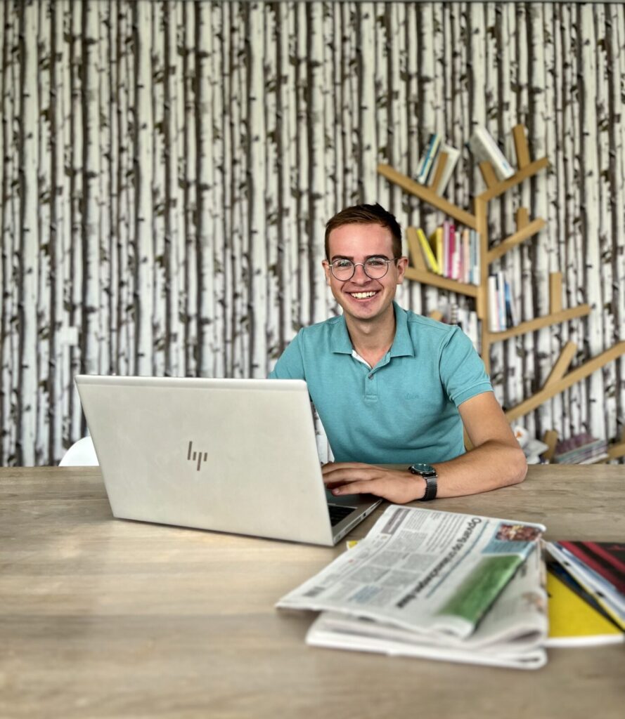 Wilmer zit achter zijn laptop. Op tafel liggen kranten.