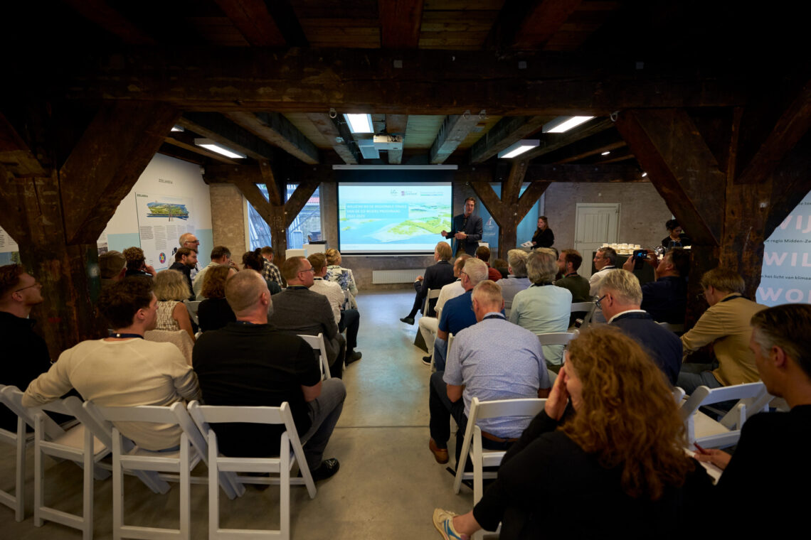 Een man geeft een presentatie voor een volle zaal tijdens de Eo Wijers Prijsvraag van Zuidwestelijke Delta