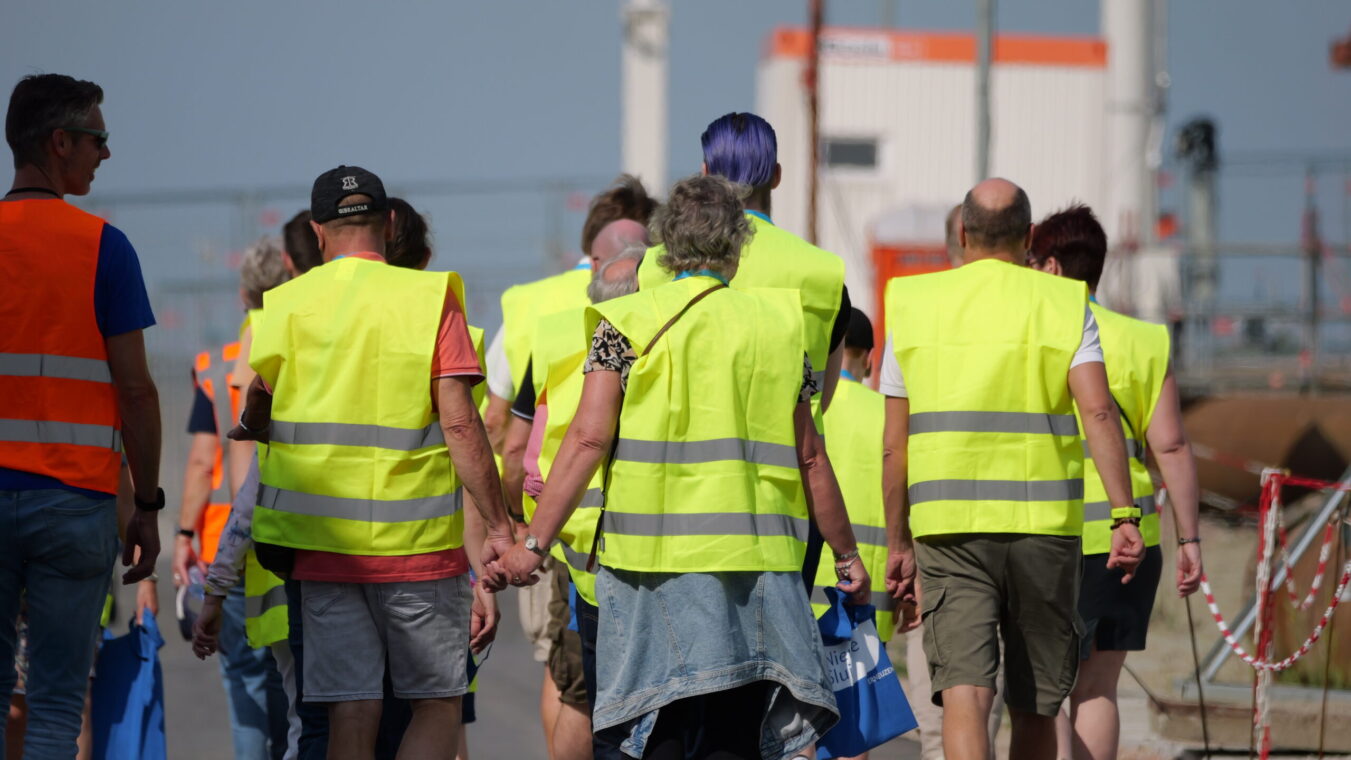 Mensen met gele hesjes lopen over het bouwterrein van de Nieuwe Sluis Terneuzen. Een man en vrouw lopen hand in hand