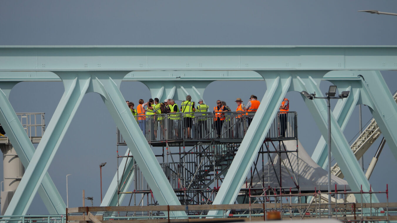 Mensen in gele en oranje hesjes staan op een uitkijkplatform bij de Nieuwe Sluis Terneuzen