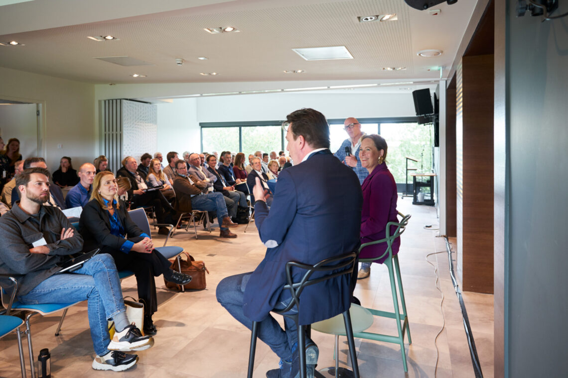 Mensen luisteren aandachtig naar sprekers voorin de zaal