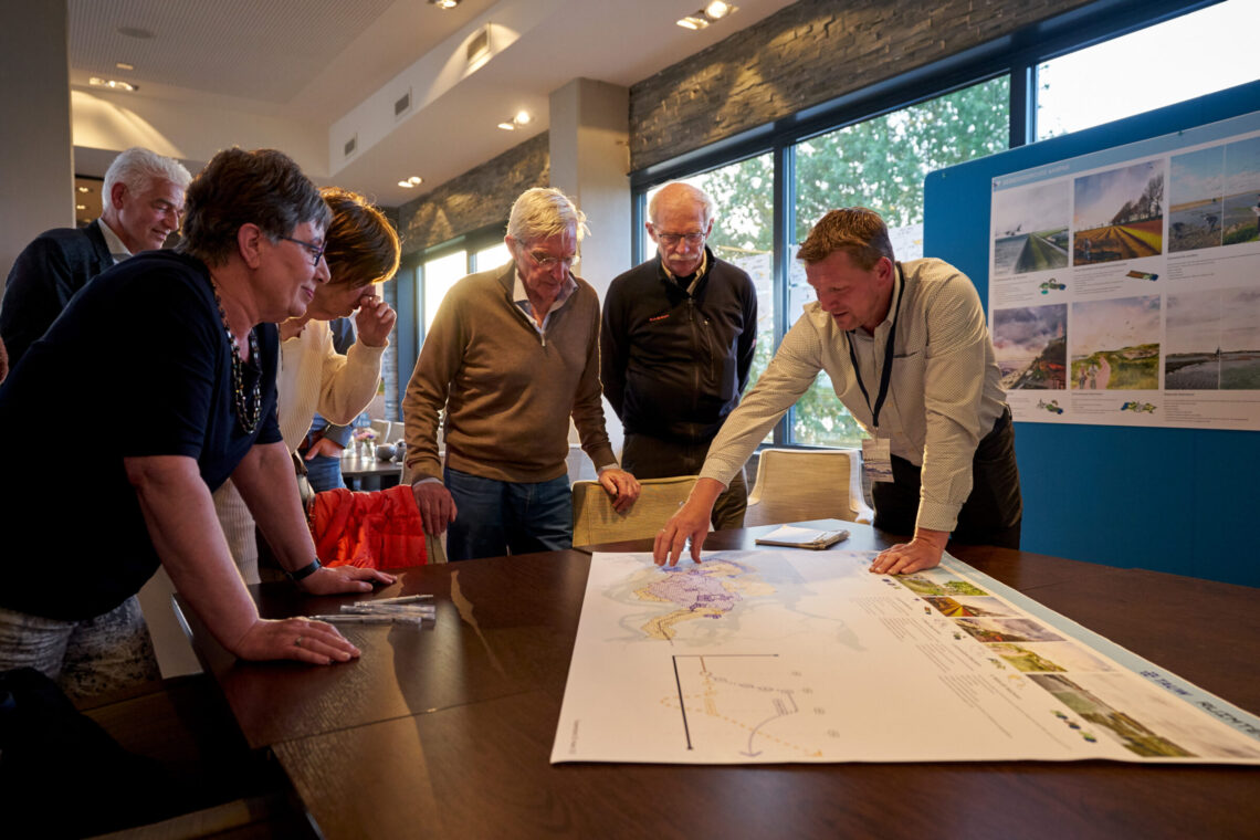 Mensen staan rondom een tafel met een landkaart. Eén man geeft uitleg