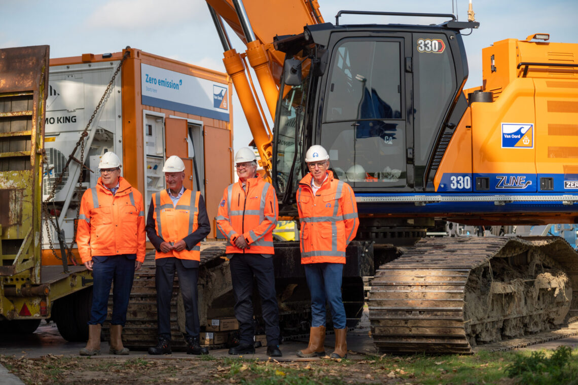 Vier mannen in werkkleding poseren voor een nieuwe elektrische kraan van aannemingsbedrijf Van Oord